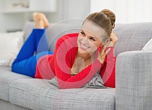 Smiling young woman laying on divan in living room