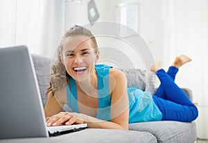 Smiling young woman laying on sofa and using laptop