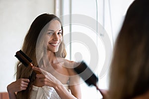 Smiling young woman look in mirror brushing hair