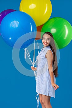 Smiling young woman looking camera and holding colorful air balloons isolated over blue