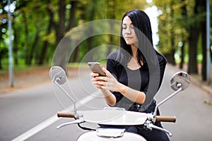 Smiling young woman looking at her mobile phone, sitting on scooter
