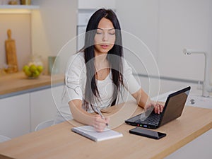 smiling young woman looking at laptop screen at kitchen