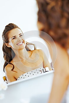 Smiling young woman looking in mirror in bathroom