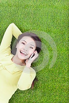 Smiling young woman lying with cell phone on green meadow