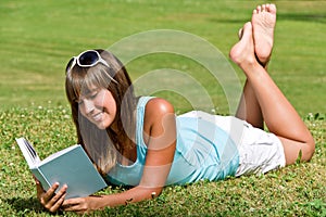 Smiling young woman lying down on grass with book