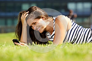 Smiling young woman lying on grass using mobile phone