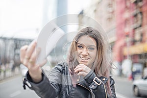 Smiling young woman makes photo phone in the street.