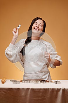 Smiling young woman making baking dough over yellow background.