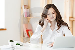 Smiling young woman making notes while talking with custumer on the phone at the call center