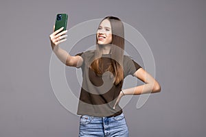 Smiling young woman making selfie photo on smartphone over gray background