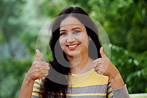 Smiling young woman making thumb up gesture at outdoors