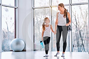 Smiling young woman and man with spots bag and mat wearing sportswear and chatting while walking in corridor of fitness center photo