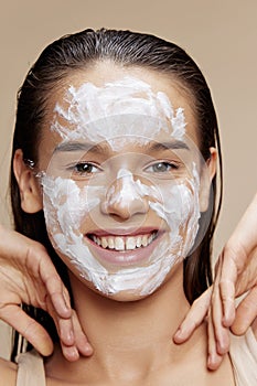 Smiling young woman with moisturizer on the cheeks in the eye area beige background