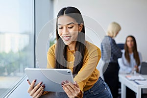 Smiling young woman at office work using digital tablet