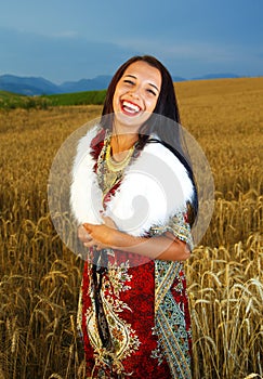 Smiling Young woman with ornamental dress standing on a wheat field with sunset. Natural background..