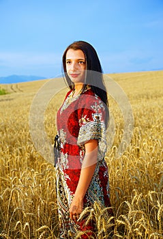 Smiling Young woman with ornamental dress standing on a wheat field with sunset. Natural background..