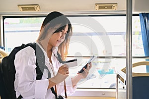 Smiling young woman passenger holding credit card and using mobile phone while traveling by bus