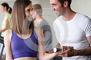 Smiling young woman and personal trainer with dumbbells in gym