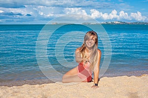 Smiling young woman in pink swimsuit throwing sand on the tropical beach