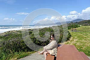 A smiling young woman posing for a photo with beautiful views of the oregon coast and vast pacific ocean in the background