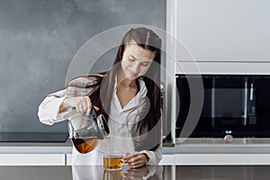 Smiling young woman pouring herbal tea in cup