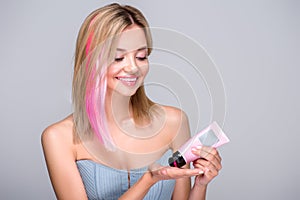 smiling young woman pouring pink coloring hair tonic on hand