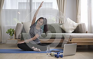 Smiling young woman practicing yoga, watching video tutorial on laptop computer at home. Healthy lifestyle, wellbeing, meditation