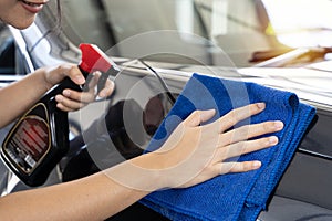 A smiling young woman with protective gloves wipes her car with a cloth ready to hit the road