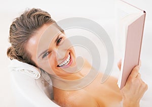 Smiling young woman reading book in bathtub