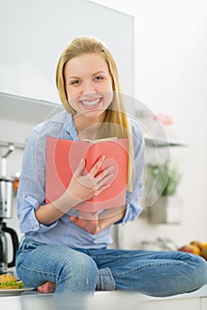 Smiling young woman reading book in kitchen