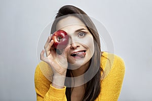 Smiling young woman with red apple. Beautiful brunette in a yellow sweater on a gray background. Healthy food and vegetarianism