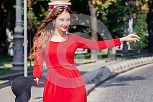 Smiling young woman in red dress is catching taxi on the city street