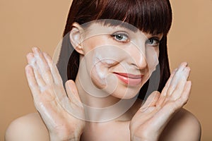 Smiling young woman with red hair washing face by natural foamy gel.