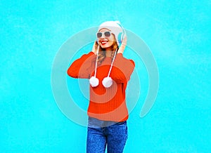 Smiling young woman in red sweater, listens to music in wireless headphones