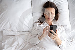 Smiling young woman relax in bed using cellphone