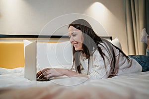 Smiling Young Woman Relaxing on Bed and Working on Her Laptop