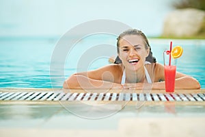 Smiling young woman relaxing in pool with cocktail