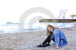 Smiling young woman rests on beach and poses in camera, sitting