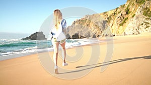 Smiling young woman running on sandy sea beach on summer vacation