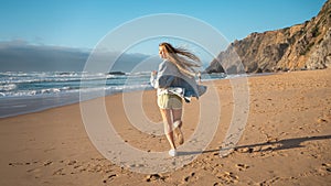 Smiling young woman running on sandy sea beach on summer vacation