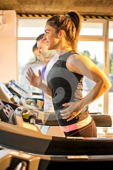 Smiling young woman running on treadmill in gym.