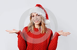 Smiling young woman in santa hat with open palms isolated on grey