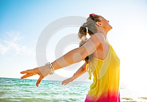 Smiling young woman on seacoast in evening rejoicing