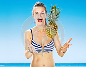 Smiling young woman on seacoast throwing pineapple up