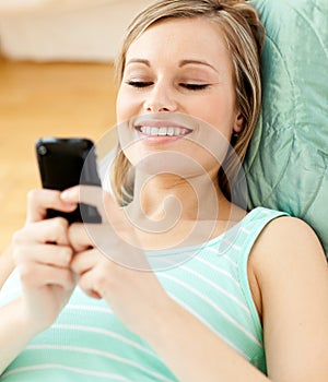 Smiling young woman sending a text lying on a sofa