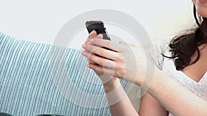 Smiling young woman sending a text sitting on a sofa