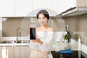 Smiling young woman showing blank smartphone screen in kitchen