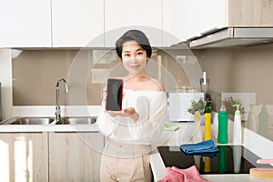 Smiling young woman showing blank smartphone screen in kitchen