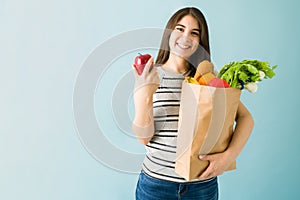 Smiling young woman showing the fresh fruits and vegetables she just bought