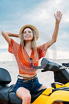 smiling young woman sitting on all-terrain vehicle in desert